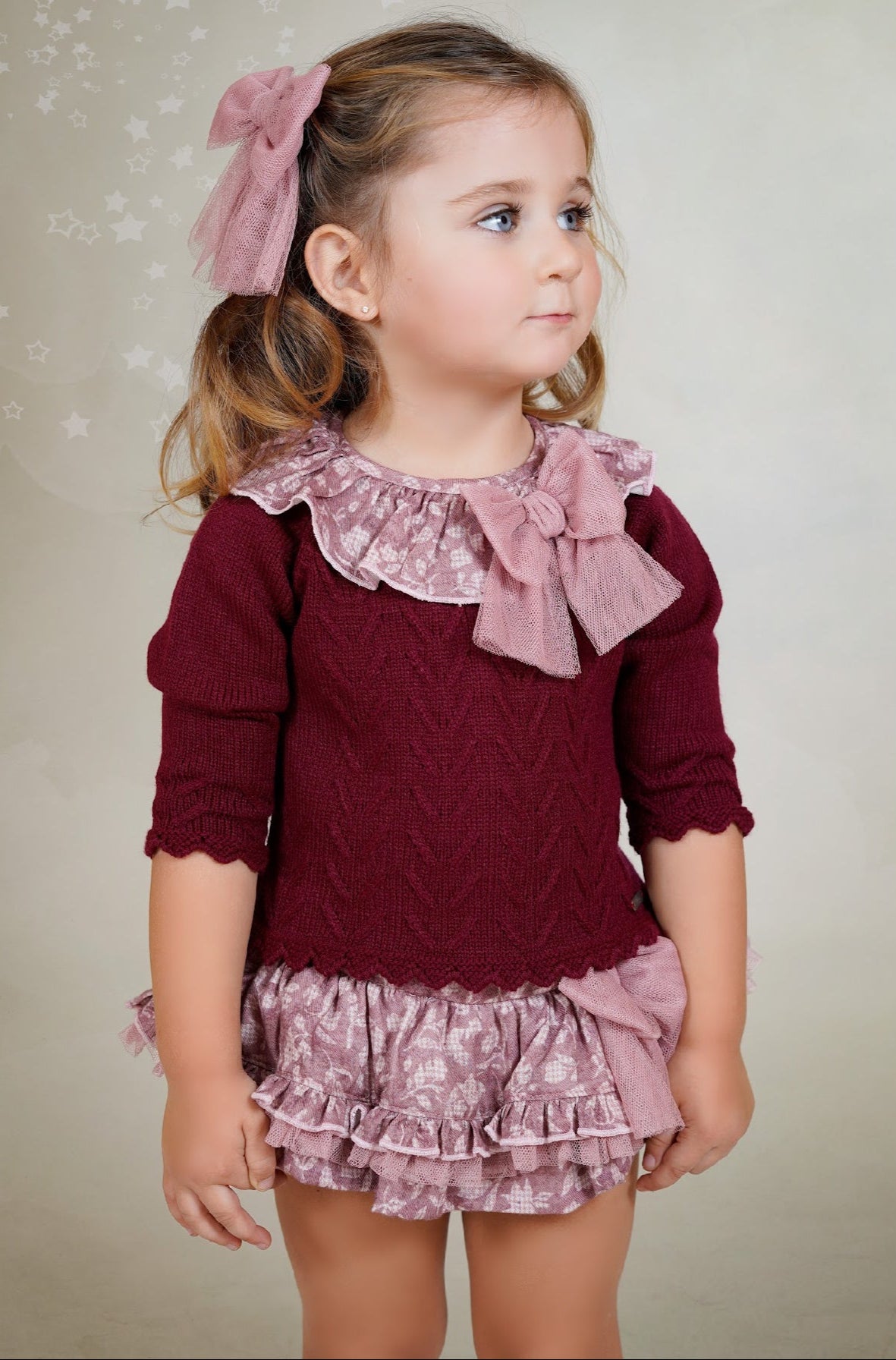 Young girl wearing a maroon top with ruffled collar and matching shorts against a neutral background