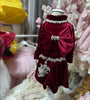Red velvet dress with decorative bow and embellishments on a mannequin against a blurred background of other dresses.
