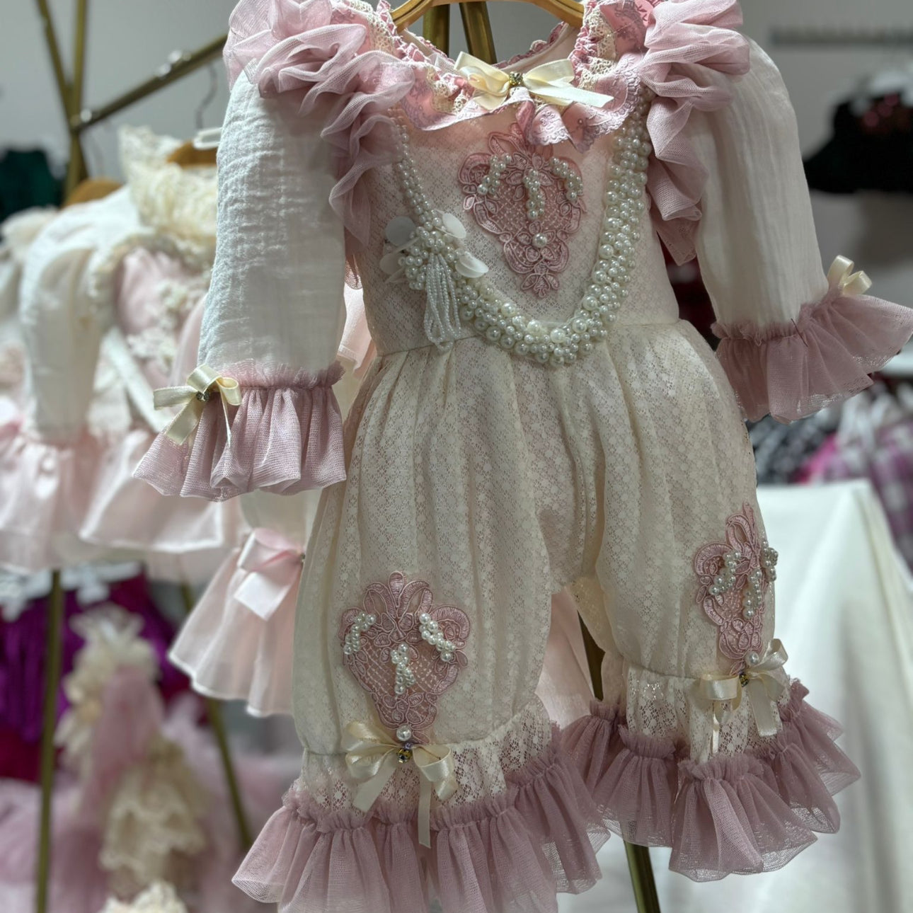 Delicate pink and white dress with ruffles and embellishments on a hanger.