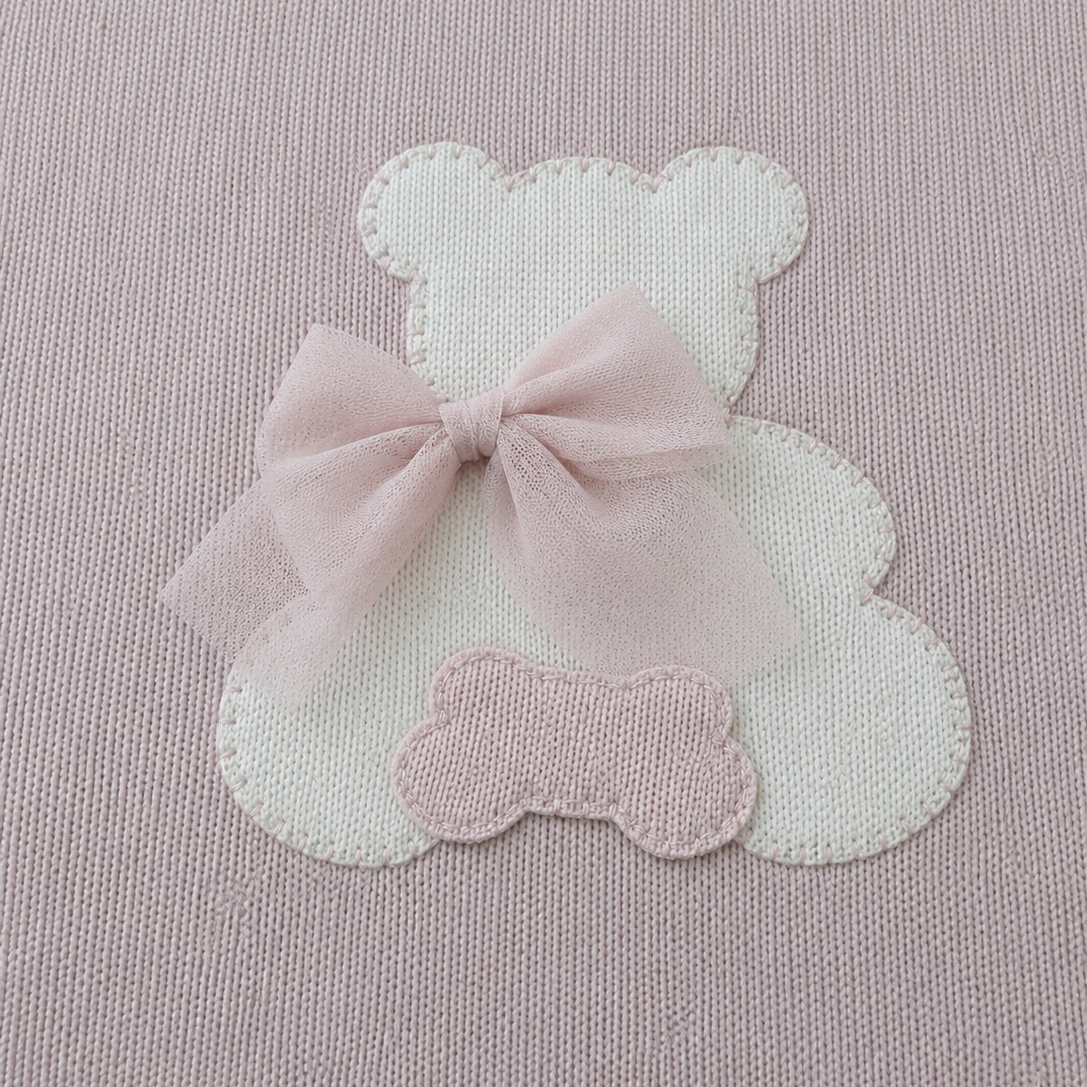 White teddy bear-shaped patch with a pink bow on a pink background