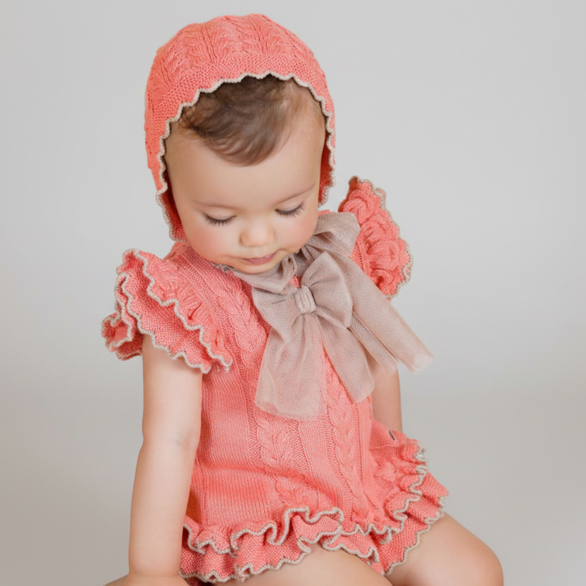 Baby in pink outfit with ruffles and a bow, wearing a matching pink bonnet, on a beige background with 'Rahigo' branding.
