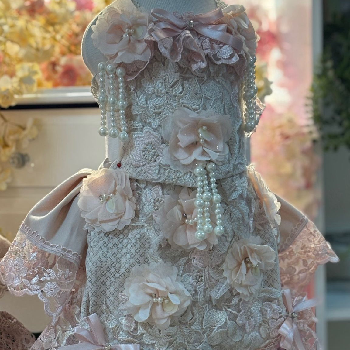 Delicate lace dress on a mannequin with floral and pearl details against a blurred floral background.